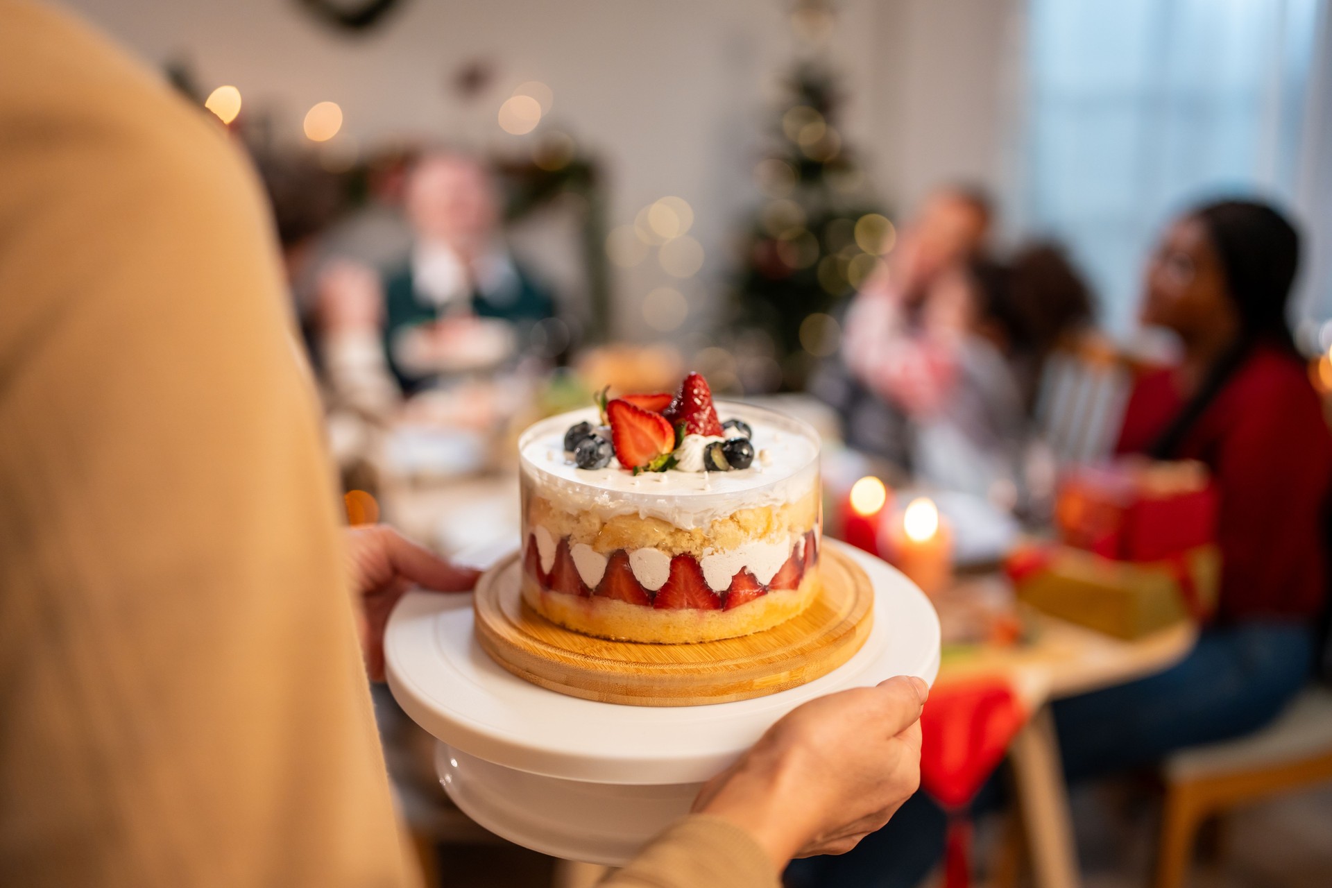 Close up of senior woman serving cake to celebrating Christmas party. Attractive diverse group of people having dinner eating food to celebrate holiday Thanksgiving, X-mas eve on dining table at home.