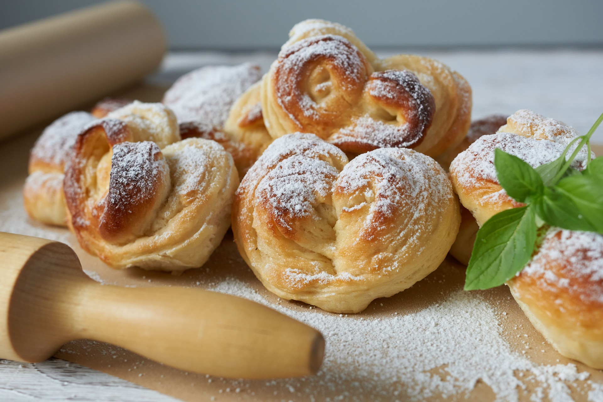 Homemade buns sprinkled with powdered sugar on a white wooden table